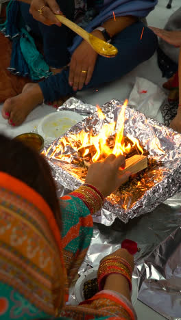 Vertikales-Video-Von-Gläubigen,-Die-Während-Der-Hinduistischen-Havan-Zeremonie-Ghee-Und-Opfergaben-Auf-Feuerflammen-Legen